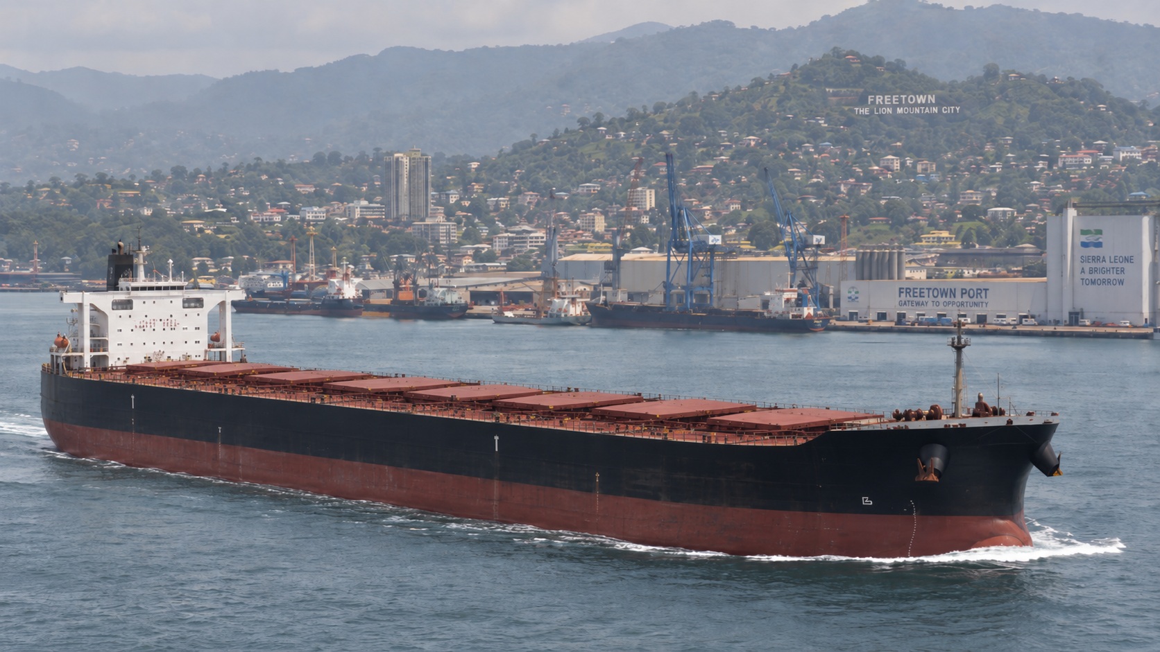 Bulk carrier sailing in front of Freetown port and the city hillside